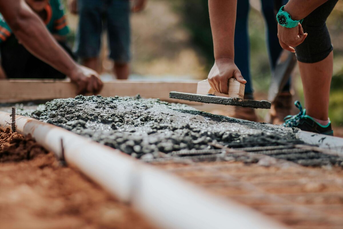 People laying self-levelling cement screed between wooden beams on the ground of a prepared construction site.