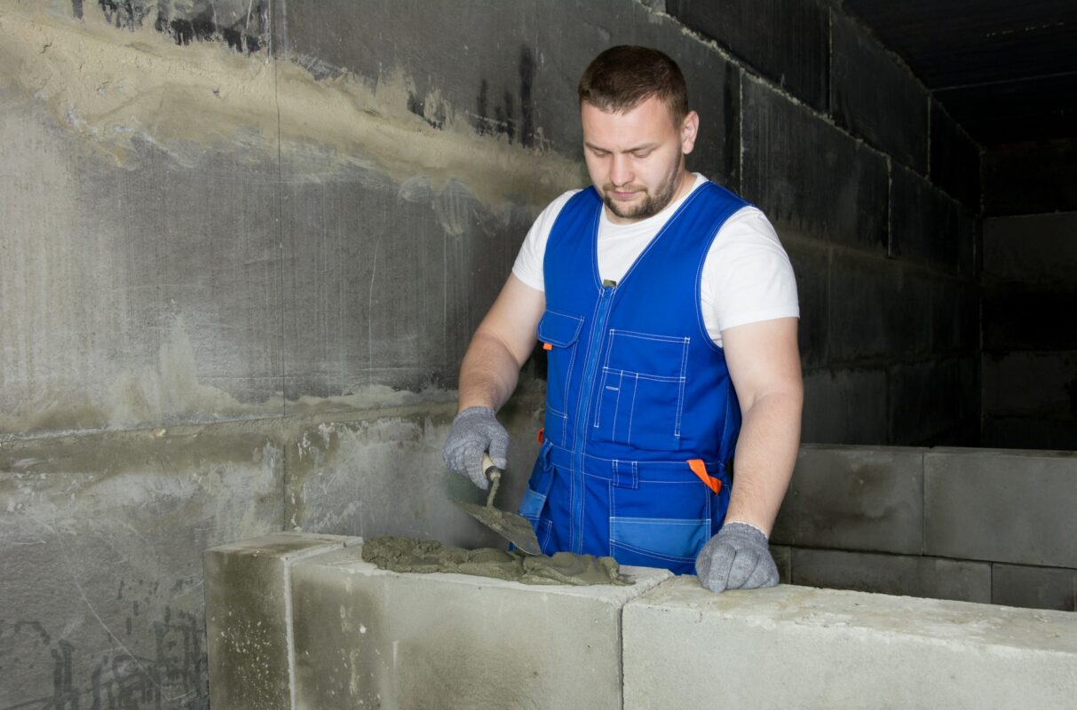 Man using a brick laying trowel to lay heavy cement bricks