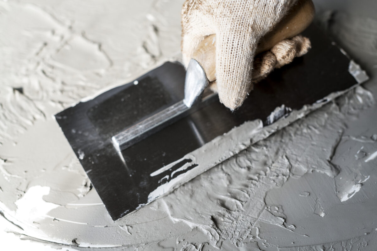 Person wearing gloves using brick trowel for plastering