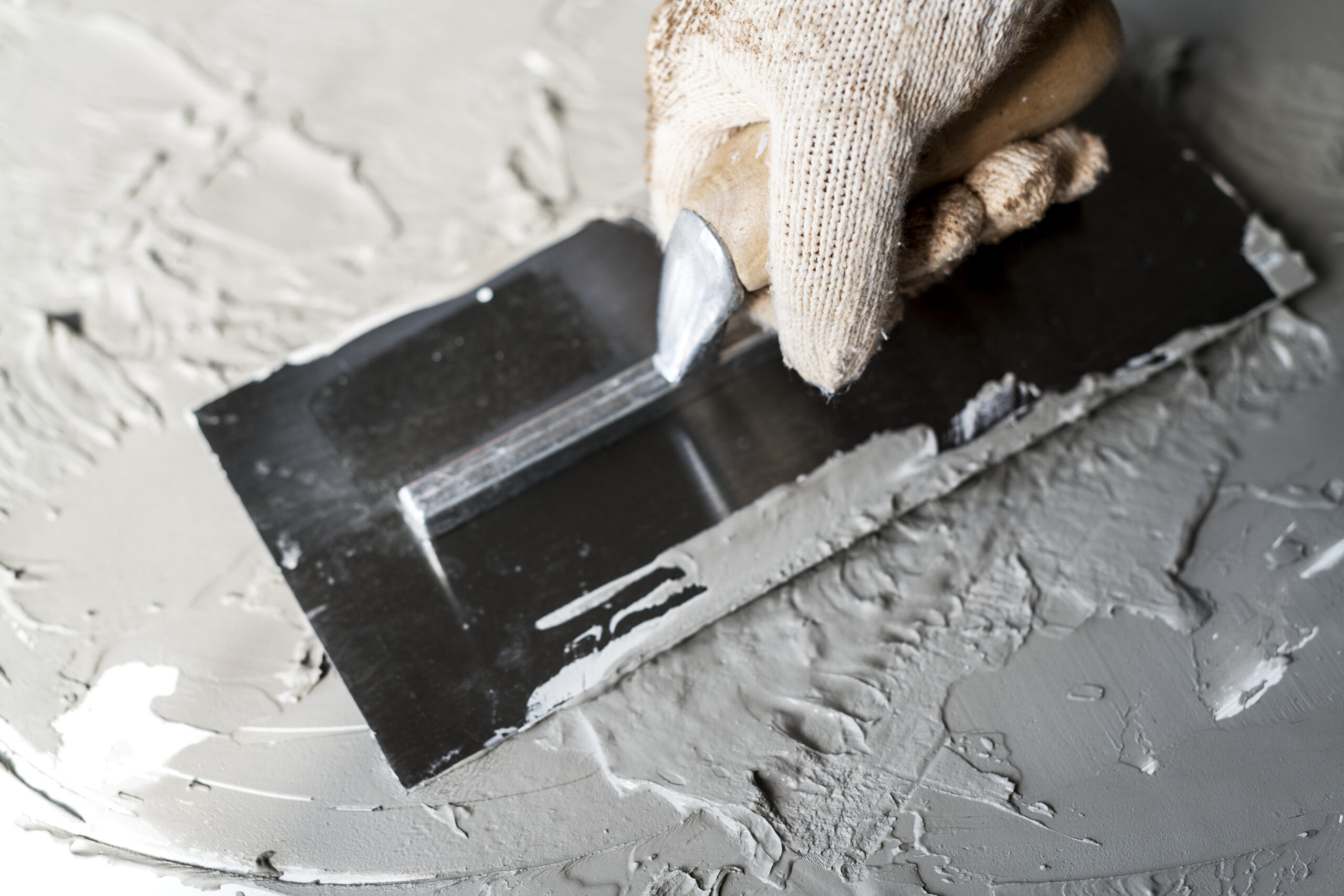 Person wearing gloves using brick trowel for plastering