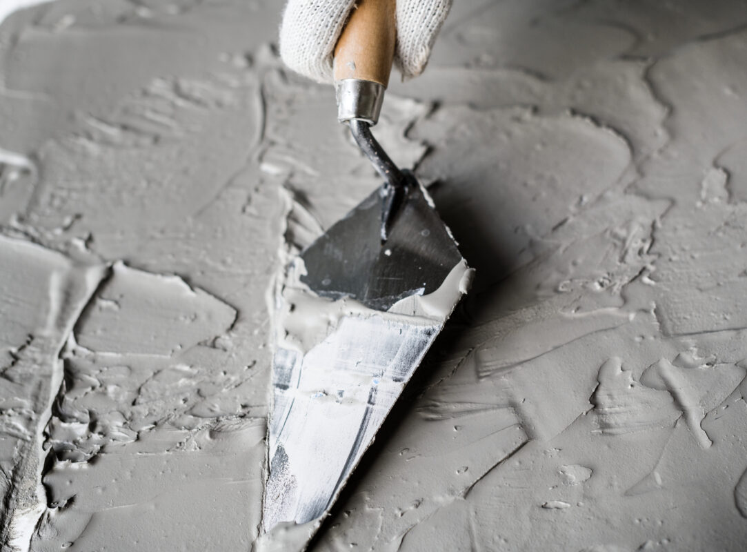 Hand of someone wearing gloves holding brick trowels from one of the best brick trowel brands spread plaster.