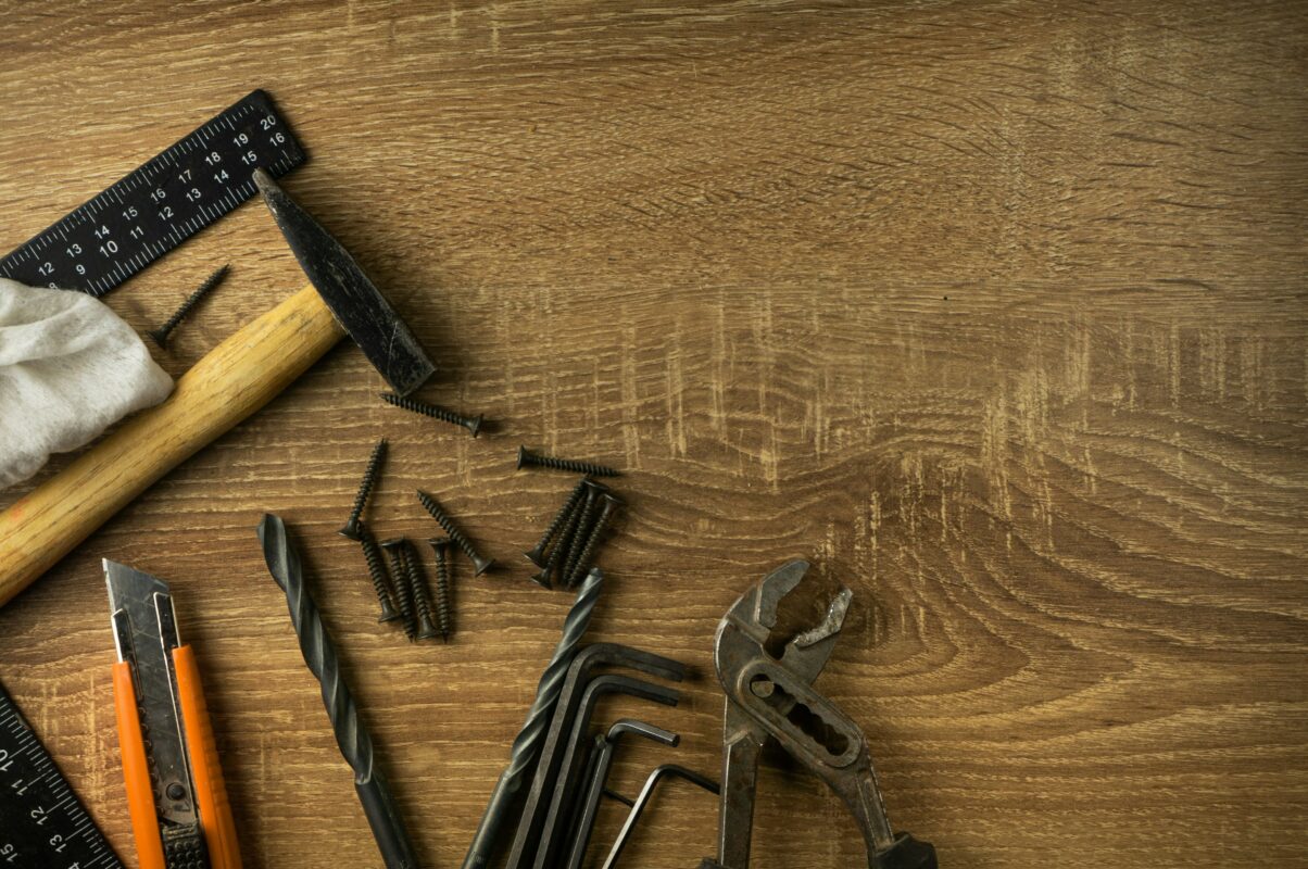 A brown handled carbon steel brick hammer on a table with other various masonry tools