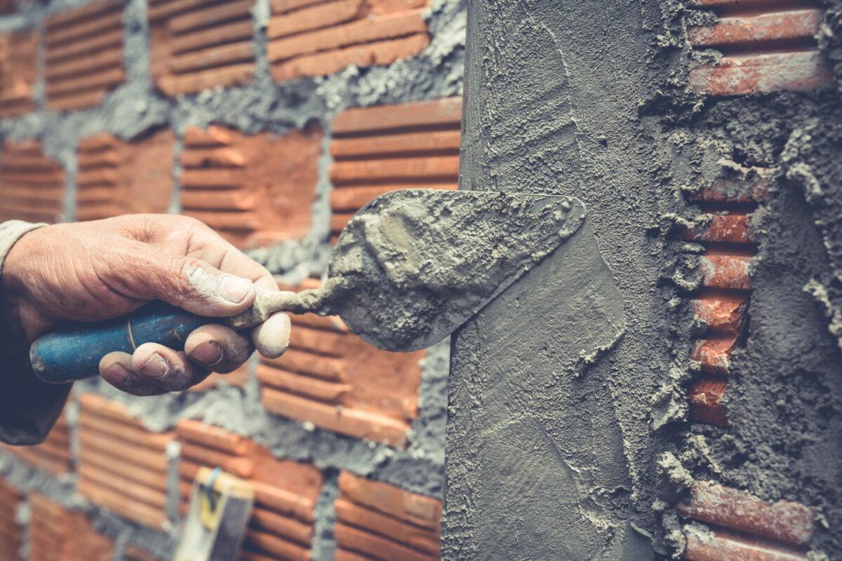 Brick trowel in use by a worker applying cement on a new brick wall