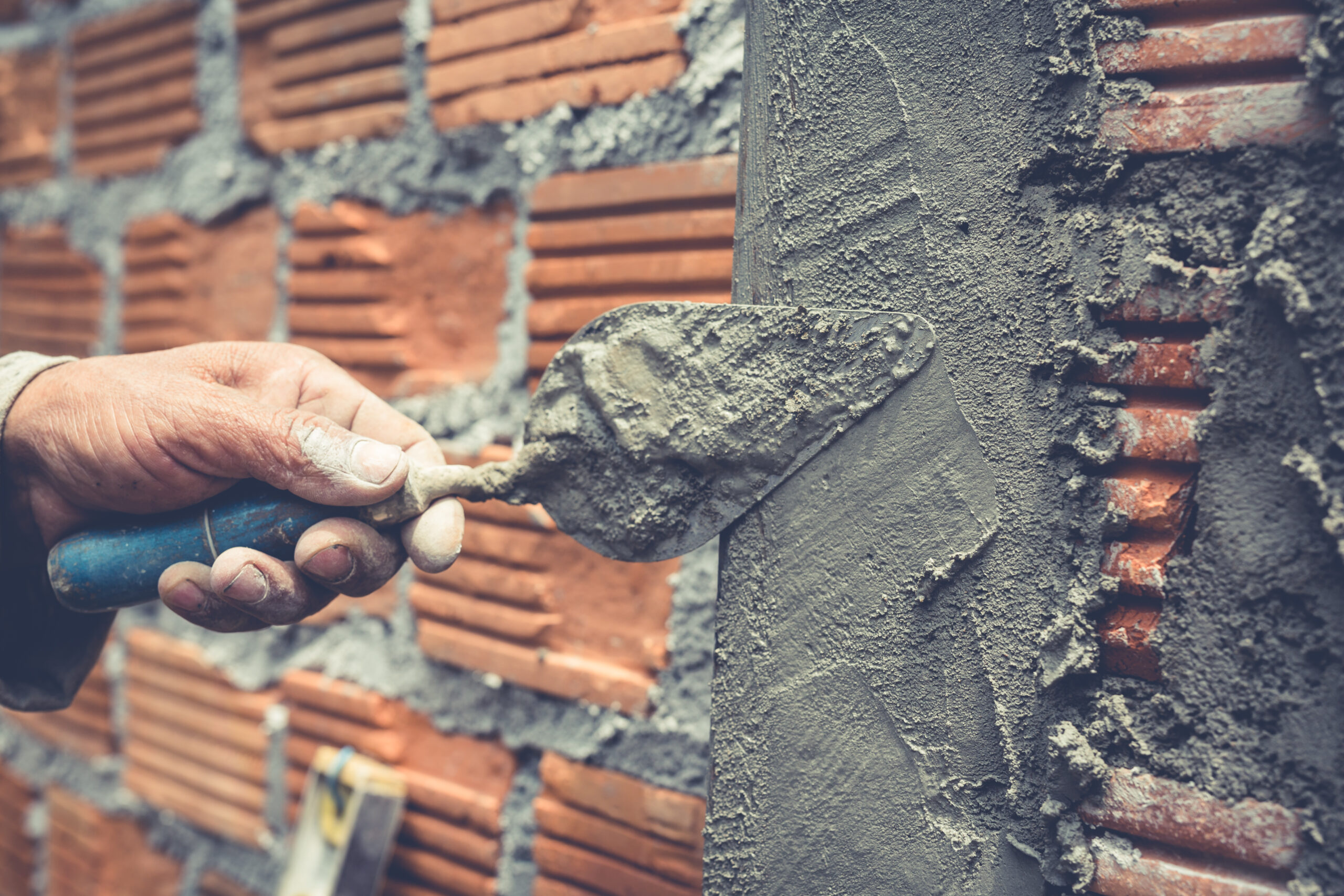Brick trowel in use by a worker applying cement on a new brick wall